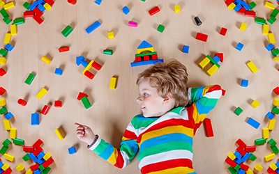 Little blonde child playing with colorful wooden blocks indoor child laying around colorful blocks