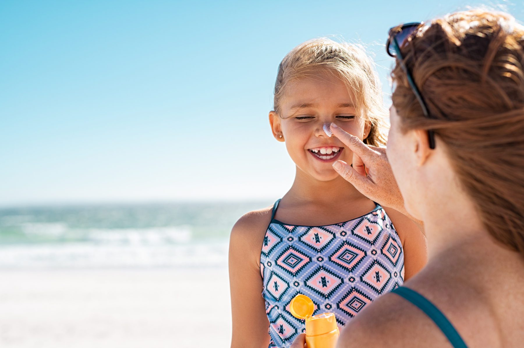 Mother applying suntan lotion on daughter's face