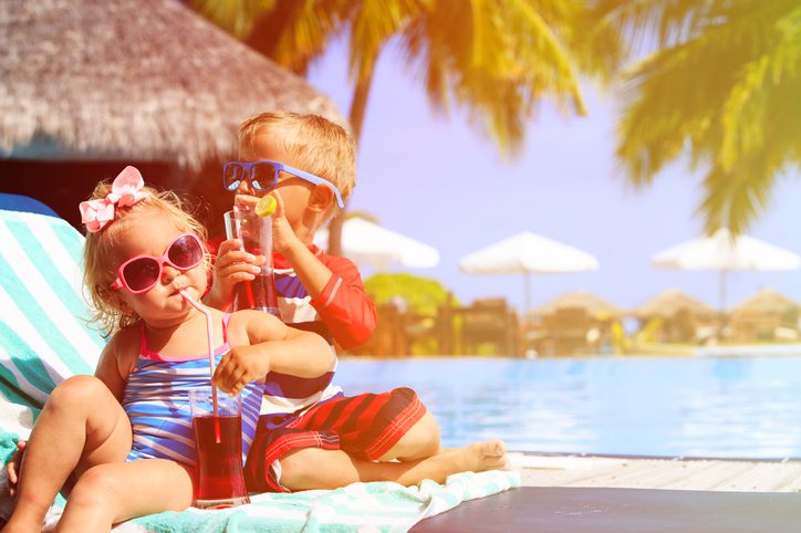 Kids relaxing at beach resort and drink juices, family vacation