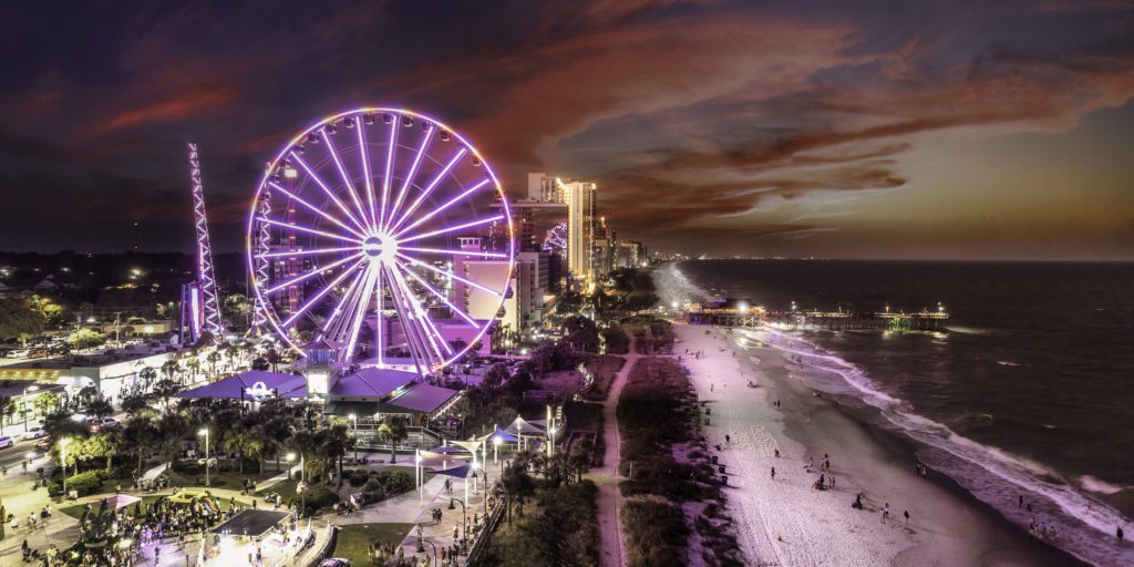 Myrtle Beach Skywheel lite up at night with a local concert happening next to it. 