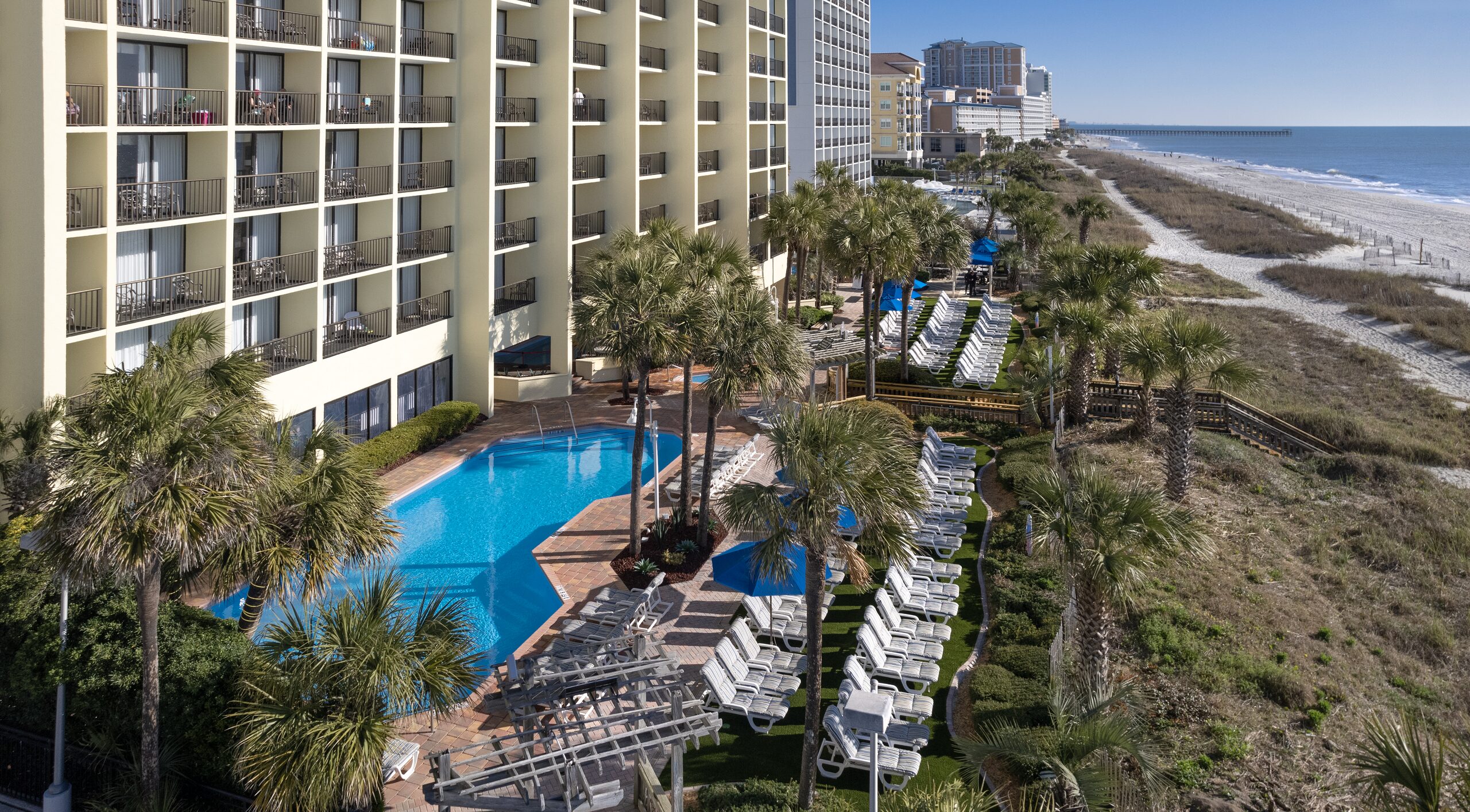 Aerial view of a multi-story hotel with a pool and beach access.