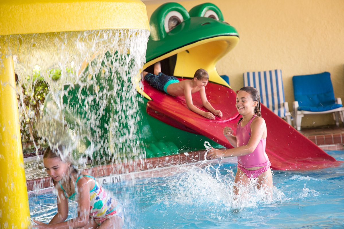 A boy slides down the tongue of the "Freddy the Frog" waterslide as other children play in the fountains