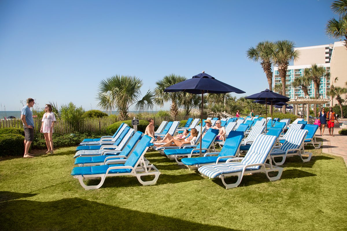 People enjoy rows of padded lounge chairs and umbrellas on the beach-view lawn outside of Sea Crest Resort