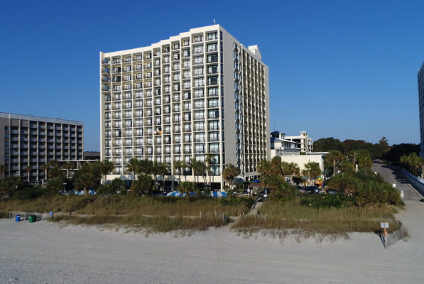 A view from the beach, of Sea Crest Resort behind grassy dunes